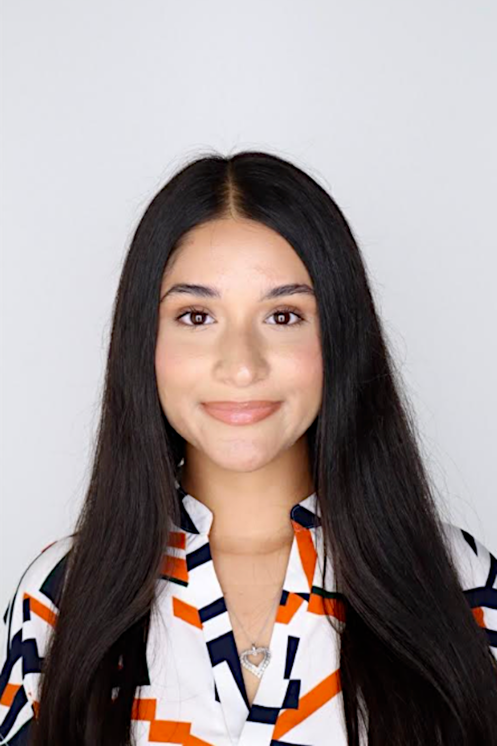 An image of Arseny Acosta, director and founder of Youth International. She has long, straight brown hair and wears a geometric patterned white, orange and black blouse.