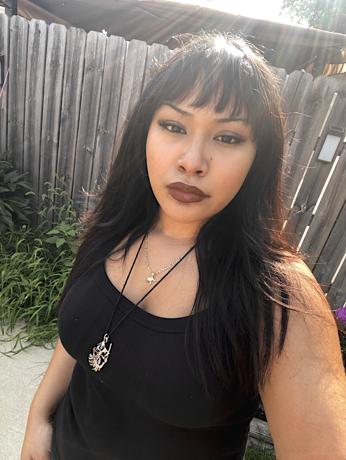 A selfie of Marian Dones, Organizational Designer of Youth International. They have long, straight brown hair and wear a ribbed black tank top and layered necklaces.